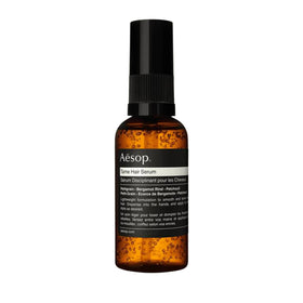 Aesop Tame Hair Serum bottle smoothing flyaways for a sleek look.