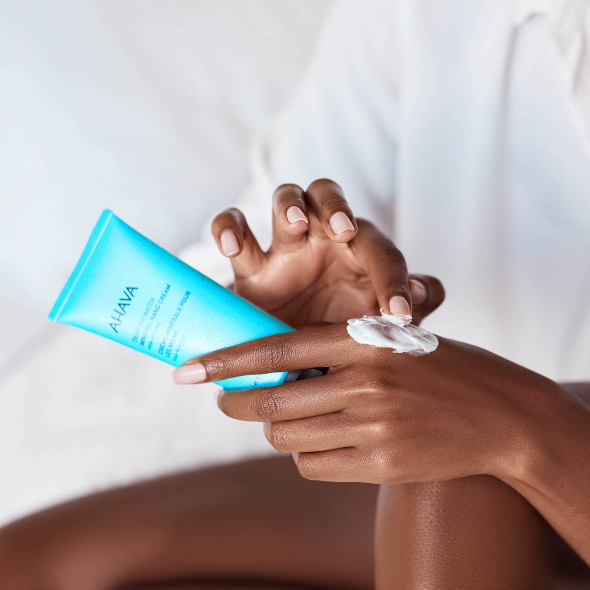 Hand applying AHAVA cream showing quick-absorbing texture.