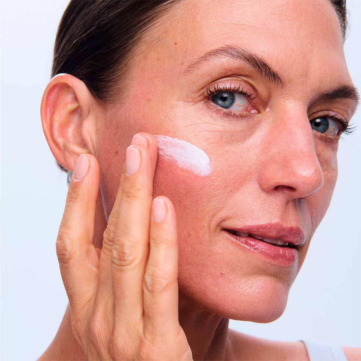 Fingertips applying the cream to face and neck with gentle downward strokes.