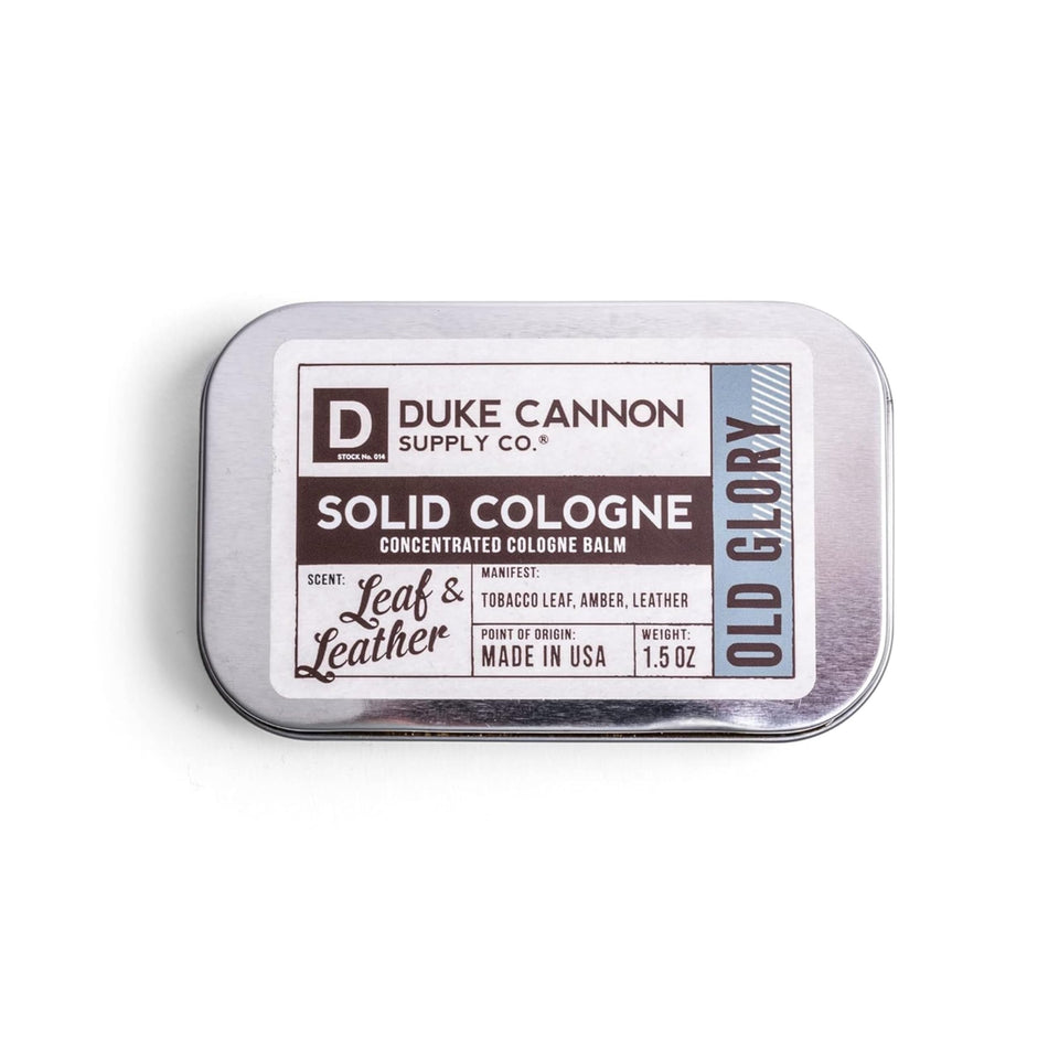 Duke Cannon Old Glory solid cologne tin label showcases premium tobacco-amber-leather scent for quick refresh.