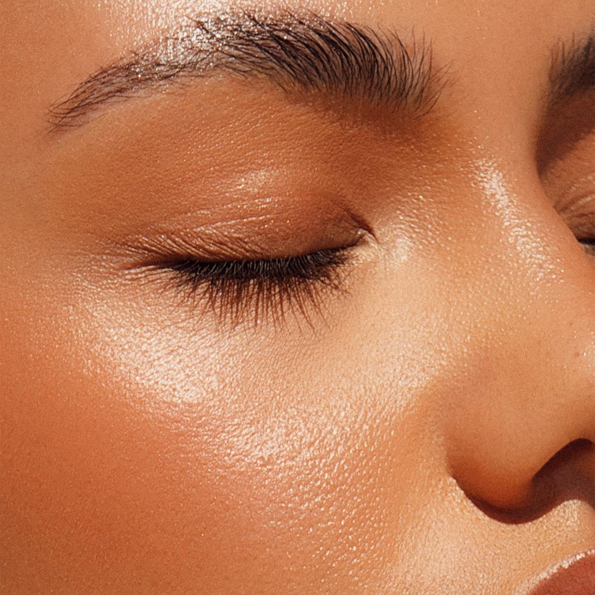 Iconic London Glow All Over Melting Balm Stick swatch on cheek for dewy radiance.