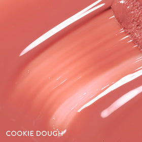Laura Geller Lip Gloss Cookie Dough cap and tube in focus promote premium packaging appeal.