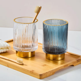 LEICURACE glass toothbrush holder with gold base on the vanity.