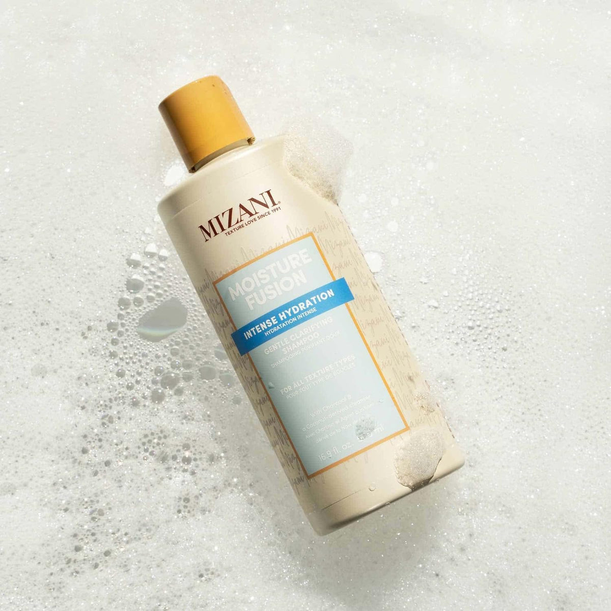 Close-up of Mizani charcoal clarifying particles lifting buildup gently.