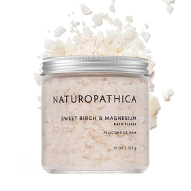 Naturopathica Sweet Birch Magnesium Bath Flakes bottle beside tub for soothing relaxation.