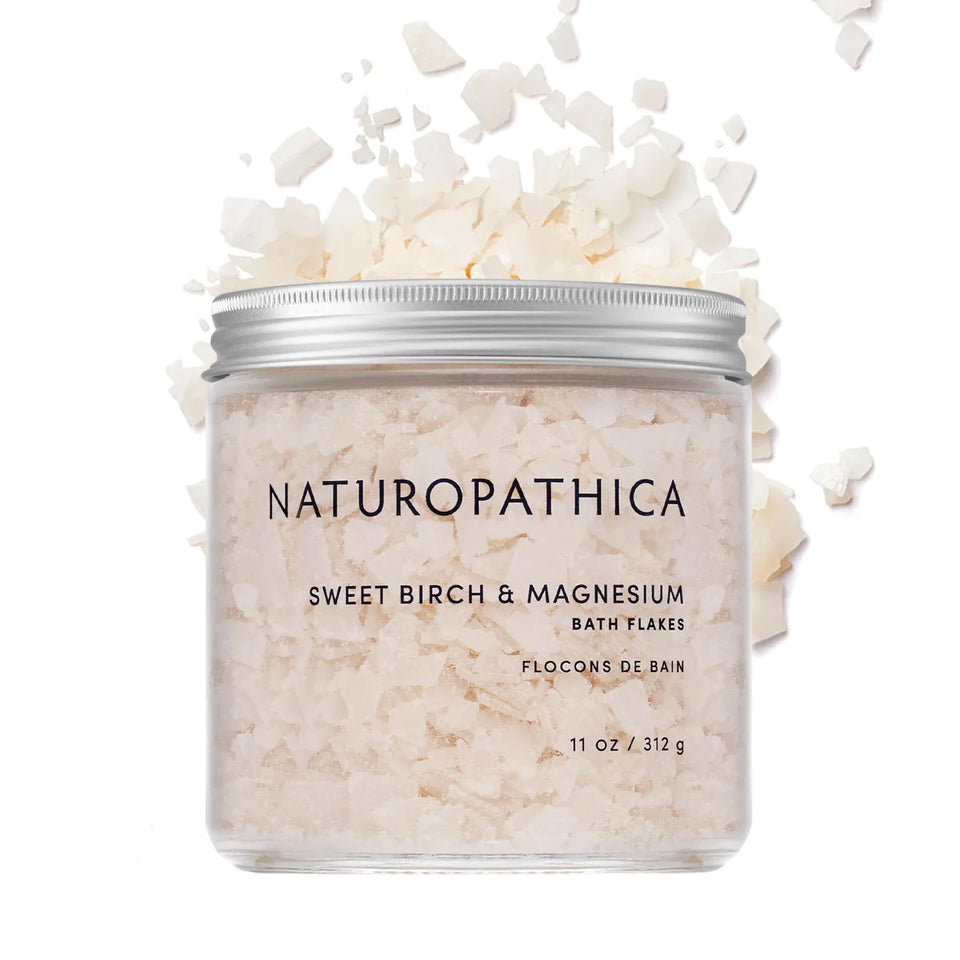 Naturopathica Sweet Birch Magnesium Bath Flakes bottle beside tub for soothing relaxation.