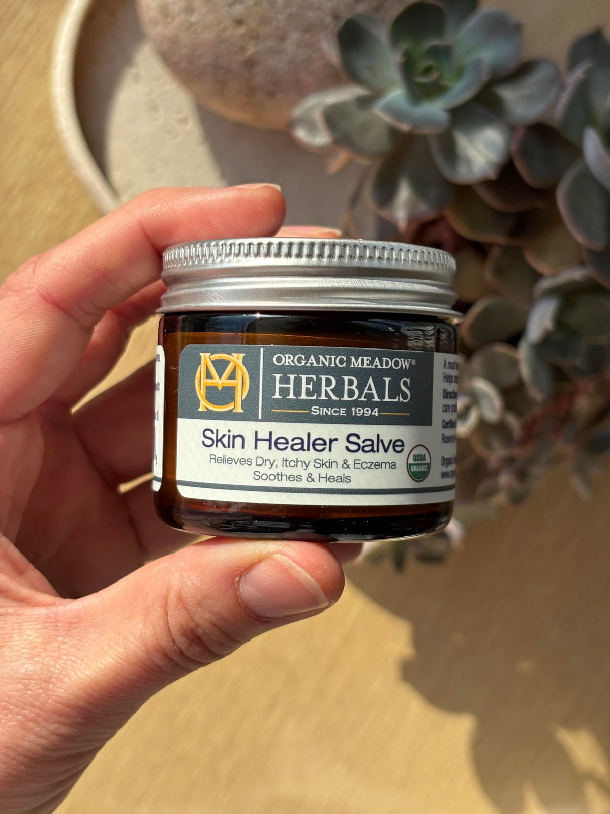 Organic Meadow Herbals Skin Healer Salve with herbs close-up supports natural care.