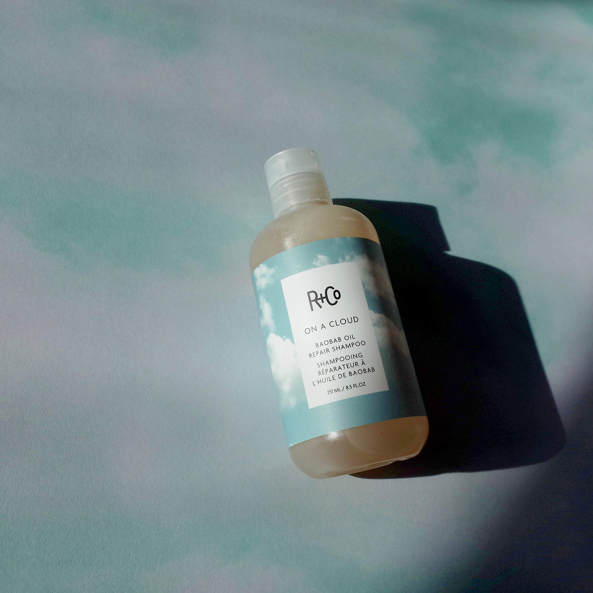 R+Co On A Cloud Baobab Repair Shampoo being applied to wet hair for gentle cleansing.
