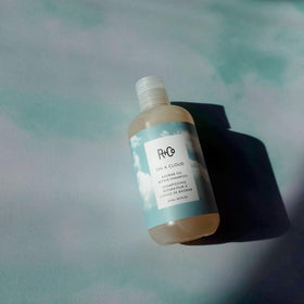 R+Co On A Cloud Baobab Repair Shampoo being applied to wet hair for gentle cleansing.
