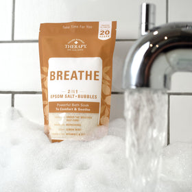 Village Naturals Therapy Breathe bath scene with foam and bubbles by the tub.